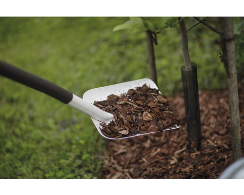 Eine Schaufel voll Rindenmulch wird um einen Baum gestreut.