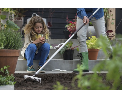 Gartenarbeitsszene mit einer Frau, die mit einem Rechen den Boden vorbereitet, während ein Kind zusieht