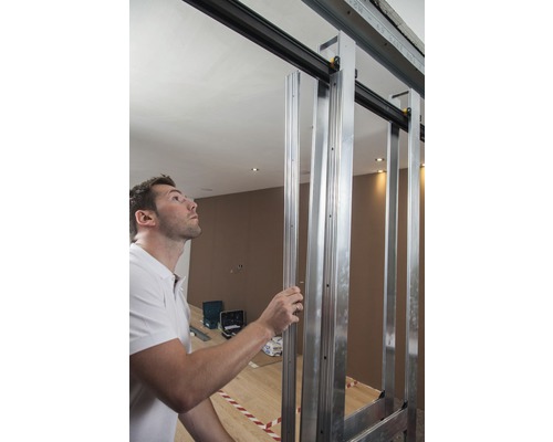 Mann montiert eine Schiebetürkonstruktion aus Metallprofilen in einem Raum.