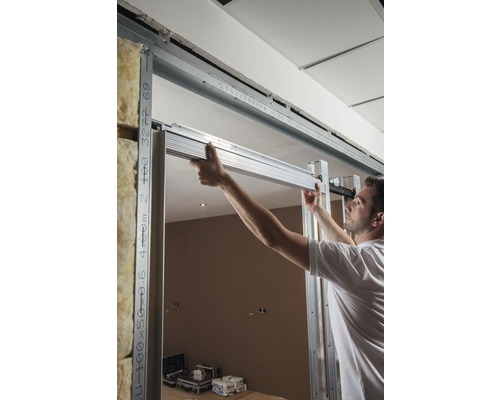 Mann montiert eine Trockenbauwand mit Metallprofilen in einem Raum.