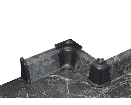 Drei schwarze Eckstücke aus Kunststoff auf einer Arbeitsplatte.