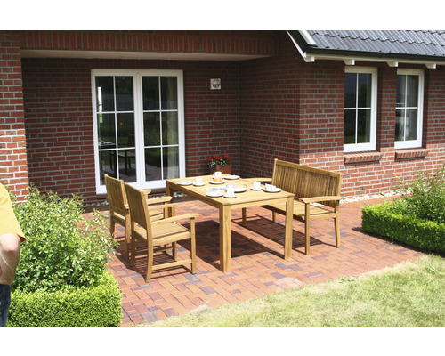 Gartenszene mit einem Holzesstisch und passenden Stühlen auf einer Terrasse vor einem Backsteinhaus.
