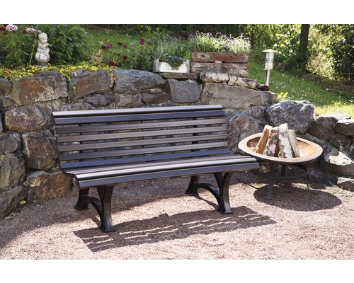 Gartenbank aus Holz und Metall vor einer Steinmauer mit Dekoration