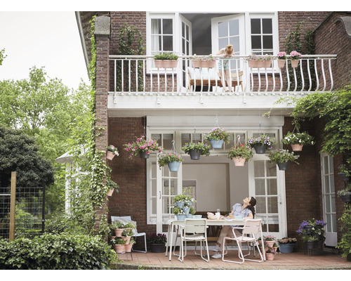 Außenansicht eines Hauses mit Balkon und Terrasse, dekoriert mit Blumenampeln und Pflanzkästen.