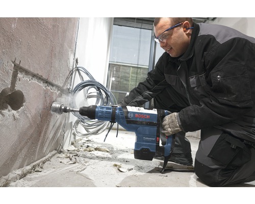 Ein Mann bohrt mit einer Bosch Schlagbohrmaschine ein Loch in eine Wand.