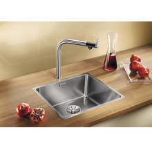 Edelstahlspüle mit Wasserhahn und Granatäpfeln auf einer hölzernen Arbeitsplatte.