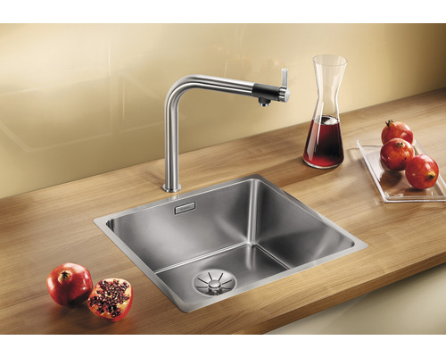 Edelstahlspüle mit Wasserhahn und Granatäpfeln auf einer hölzernen Arbeitsplatte.