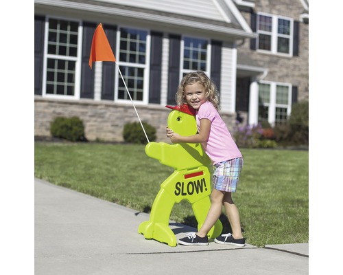 Kind umarmt ein grünes Verkehrsschild mit der Aufschrift ''Langsam!'' und einer orangefarbenen Flagge