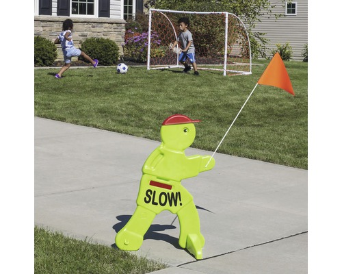 Kindersicherheitsschild mit der Aufschrift ''Langsam!'', mit Kindern die im Hintergrund Fußball spielen