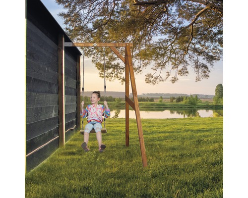 Mädchen schwingt auf einer Holzschaukel im Garten vor einem See.