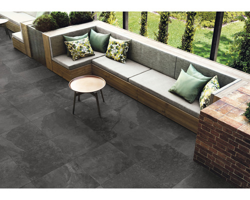Außenbereich mit grauen Bodenfliesen, Sitzgruppe mit Kissen und kleinem Tisch