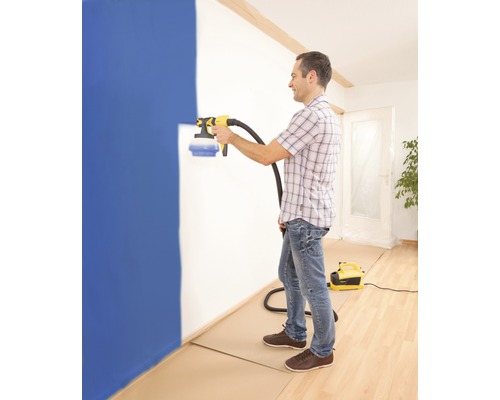 Ein Mann verwendet ein Farbsprühgerät, um eine Wand in einem Raum zu streichen.