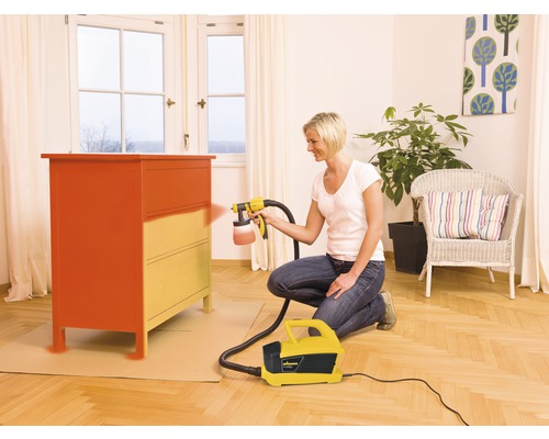 Frau lackiert Kommode mit Farbsprühsystem in einem Wohnraum.