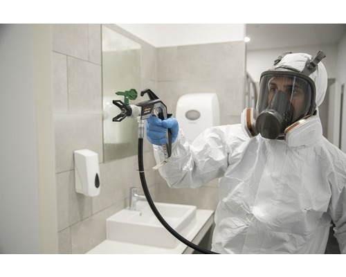 Eine Person in Schutzkleidung verwendet ein Farbspritzgerät in einem Badezimmer.