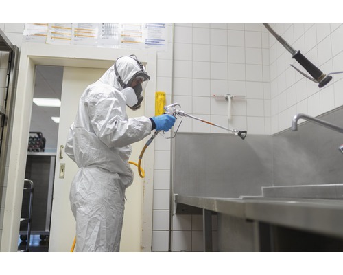 Eine Person in Schutzkleidung sprüht eine Oberfläche mit einem Sprühgerät