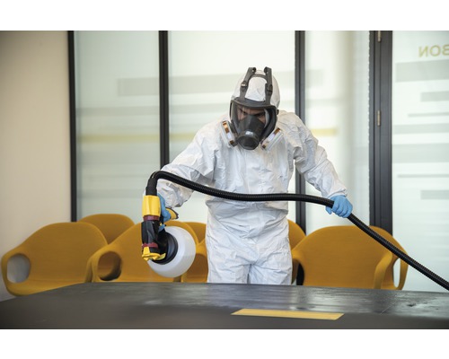 Eine Person in Schutzkleidung desinfiziert einen Raum mit einem Sprühgerät.