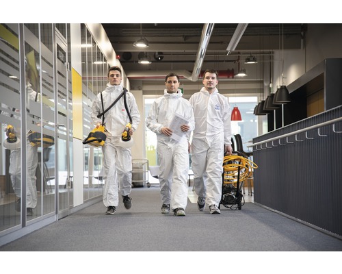 Drei Personen in Schutzanzügen gehen in einem Büro.