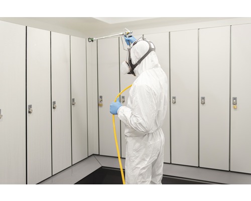 Mann in Schutzanzug desinfiziert Spinde mit Sprühgerät
