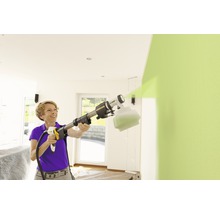 Frau benutzt Farbsprühsystem zum Streichen einer Wand im Innenbereich.