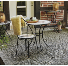 Gartenszene mit Mosaiktisch, Stuhl mit Fellauflage und Dekoration im Außenbereich