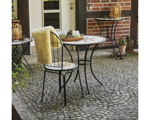 Gartenszene mit Mosaiktisch, Stuhl mit Fellauflage und Dekoration im Außenbereich