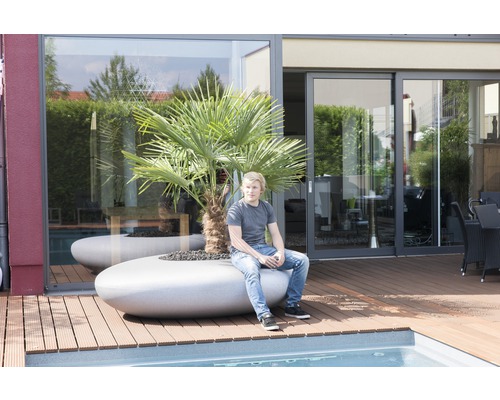 Außenbereich mit Pool und Mann, der auf einem Pflanzkübel mit Palme sitzt