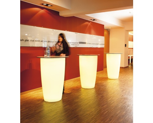 Drei beleuchtete Stehtische in einem Raum mit einer Person an einem Tisch