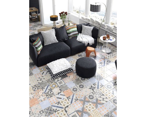 Wohnzimmer mit Sofa, Kissen, Hocker und Bodenfliesen im Patchwork Design für eine lebendige Atmosphäre.