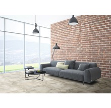 Wohnzimmer mit grauer Couch, Bodenfliesen in Steinoptik und einer Backsteinwand