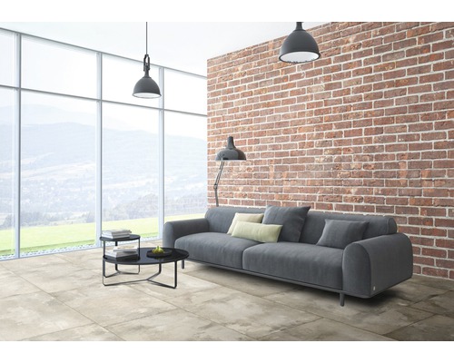 Wohnzimmer mit grauer Couch, Bodenfliesen in Steinoptik und einer Backsteinwand