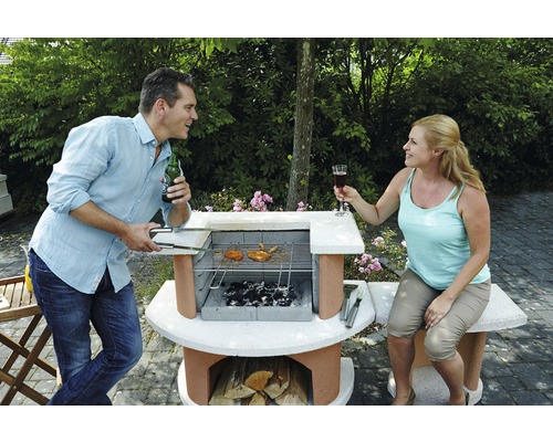 Mann und Frau grillen im Garten mit einem Steingrill und Holzkohle.