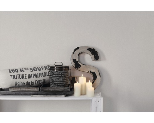 Dekoratives Arrangement mit Kissen, Behälter, Kerzen und Buchstabe auf einem Regal