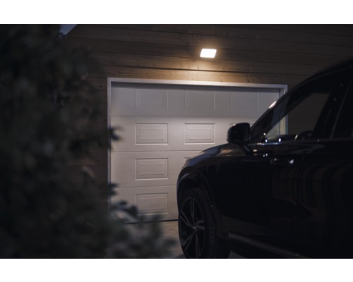 Szene mit einer Garage, beleuchtet durch eine Deckenleuchte, mit einem Auto davor.