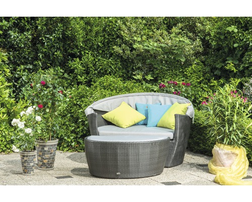 Gartenmöbel-Set mit Rattan-Optik und farbigen Kissen vor grüner Hecke