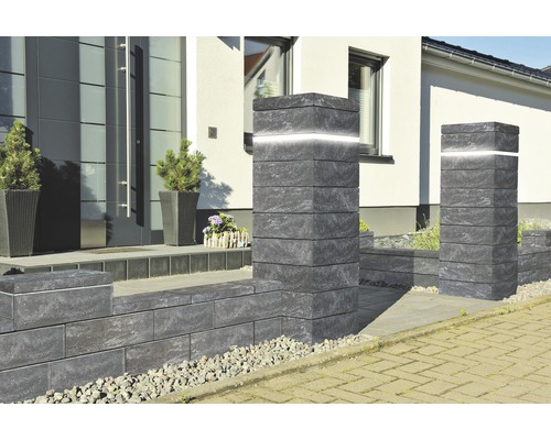 Eingangsbereich mit Pflastersteinen, Mauerelementen und beleuchteten Säulen