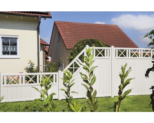 Gartenansicht mit weißem Zaun und Gartentor vor Wohnhäusern.