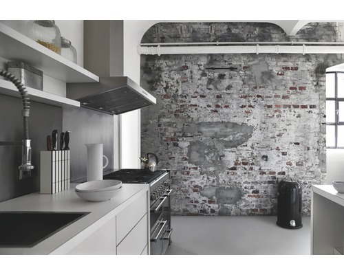 Helle Küche mit Küchenzeile, Dunstabzugshaube, Herd, Küchenutensilien und Mülleimer vor einer Backsteinwand.