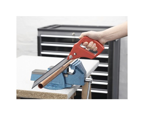 Handsäge schneidet Rohr, das in einem Schraubstock befestigt ist