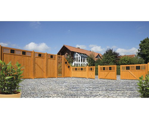Verschiedene Holzzaunelemente und Gartentore auf einer gepflasterten Fläche vor einem Haus.