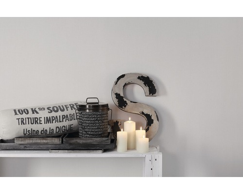 Dekorative Szene mit Kissen, Dose, Kerzen und Buchstabenornament auf einem weißen Regal.