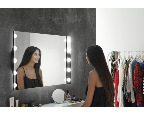 Frau vor einem beleuchteten Kosmetikspiegel im Badezimmer.