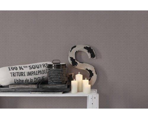 Dekorative Szene mit Kissen, Dose, Kerzen und einer großen Buchstaben-Skulptur vor einer gemusterten Wand.