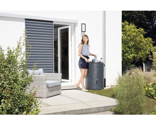 Frau gießt Pflanzen mit Regenwasser aus einer Regentonne im Garten.