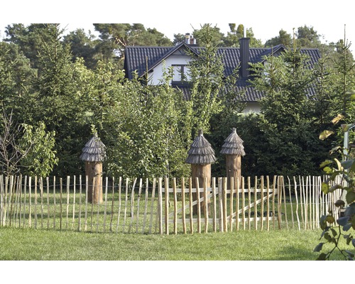 Drei hölzerne Bienenhäuser hinter einem Holzzaun in einem Garten.