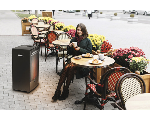Frau trinkt Kaffee auf einer Terrasse mit Heizstrahler und Blumen