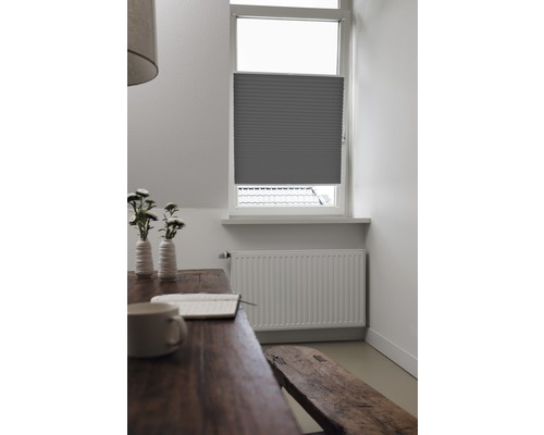 Ansicht eines Raumes mit einem Fenster, das mit einem grauen Plissee versehen ist, zusammen mit einem Holztisch und einer Bank