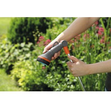 Gartenschlauch mit Sprühkopf in der Hand vor Grünpflanzen