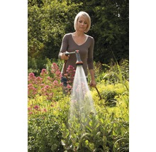 Frau gießt Pflanzen mit einem Gartenschlauch im Garten.