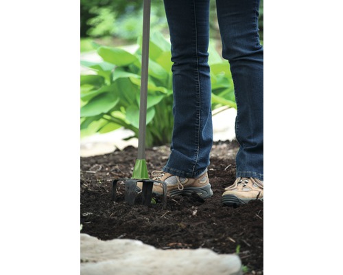 Eine Person benutzt einen Kultivator im Garten, um den Boden aufzulockern.