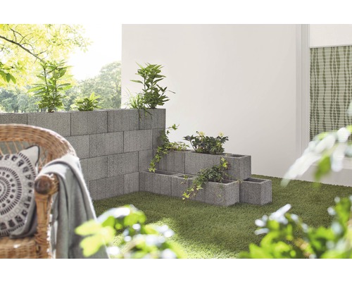 Gestapelte Betonblöcke bilden eine Gartenmauer und Pflanzkästen mit Pflanzen